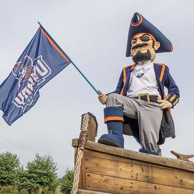 Max the Marauder standing at the front of a boat with a flag in hand.